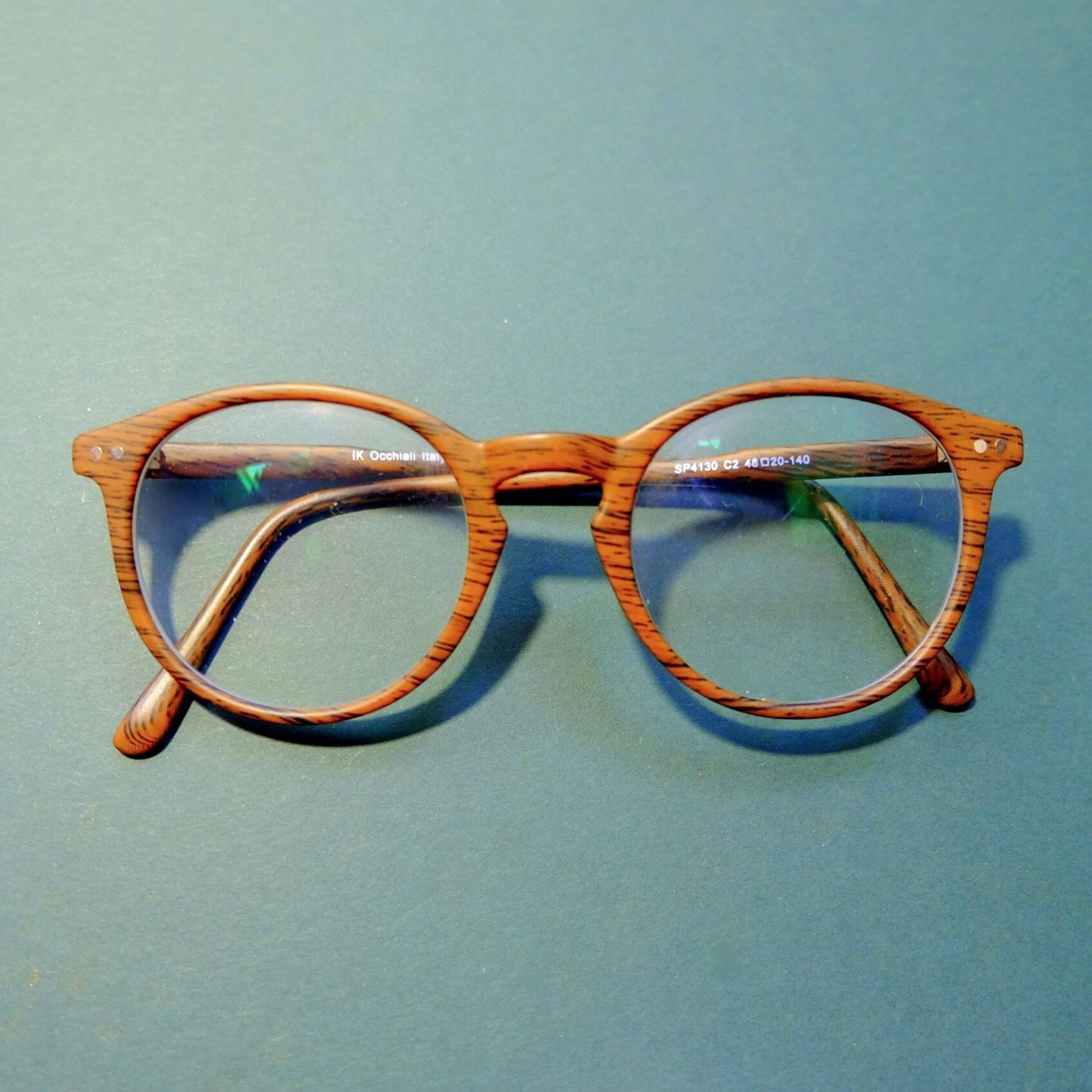 A brown pair of glasses. They are rounded, with a wooden pattern, against a light blue background.