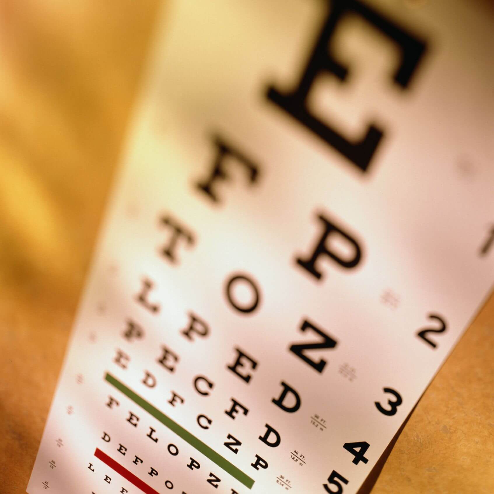 A snellen eye chart, typically used to diagnose vision problems. It is black letters of various sizes, on a white poster, in various rows, with the top letters being bigger and shrinking as you go down. It is on a beige wall.