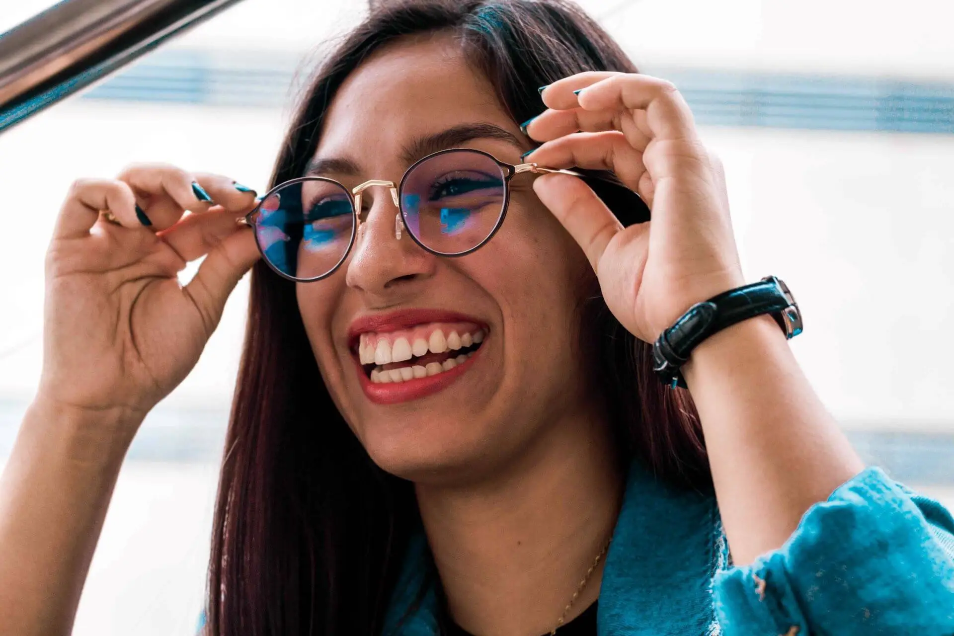 VC - Easy Sign-up Eye Exams A hispanic woman holds a new pair of eyeglasses with progressive lenses to check her vision. she is wearing red lipstick, has white teeth, and is smilling.